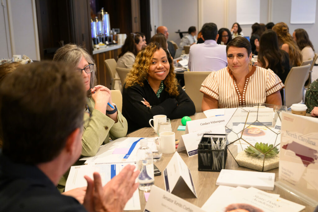 A group of individuals engage in discussion at a conference table, with name cards and materials visible, suggesting a professional or academic setting.