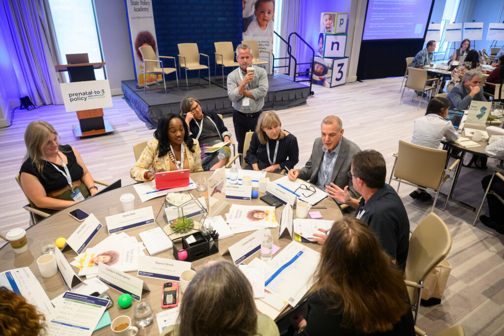 A group of professionals collaborates around a table at a conference, discussing prenatal-to-3 policy initiatives.