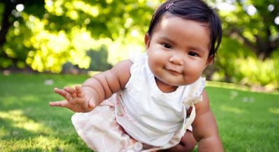 Cute baby girl with a smile on her face, reaching out to take her first crawling step on a lush green lawn at an outdoor park