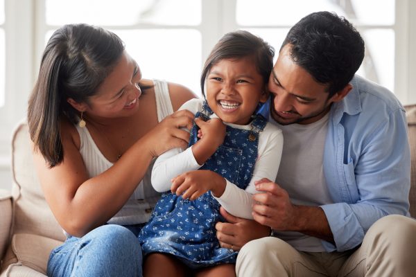 Family photo of a young couple smiling and laughing while bonding with their daughter on the sofa at home