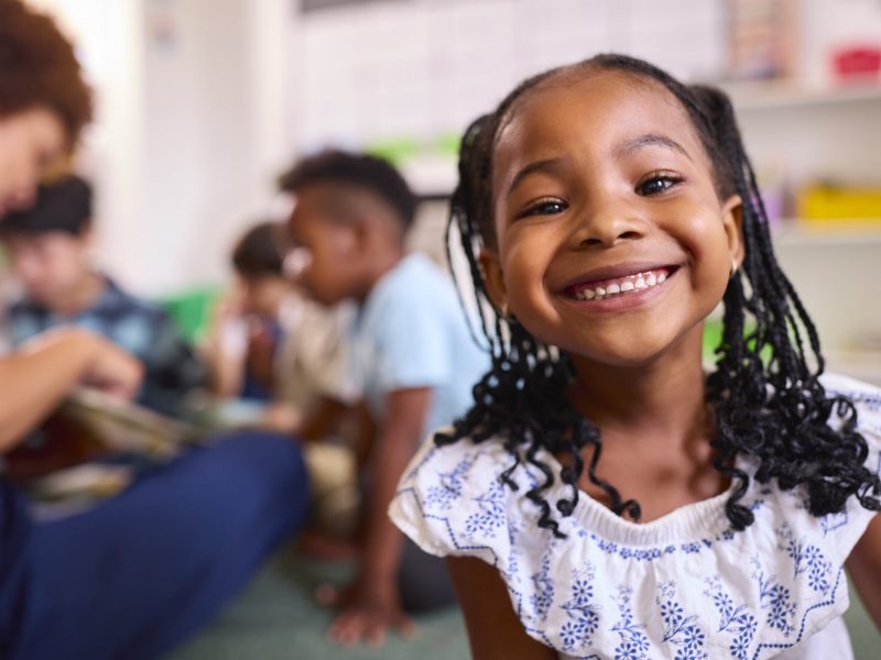 Portrait Of Smiling Female Elementary School Pupil Sitting In Classroom At School