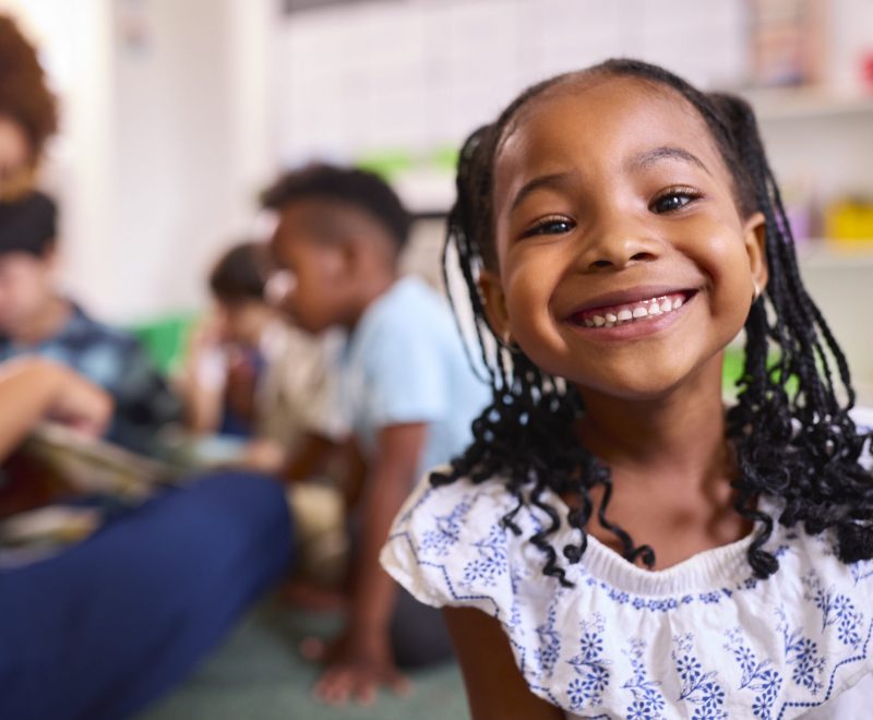 Portrait Of Smiling Female Elementary School Pupil Sitting In Classroom At School